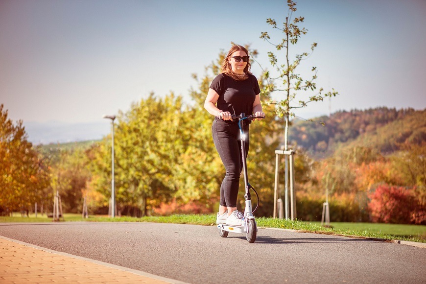 žena idúca na elektrickej kolobežke po cyklotrase
