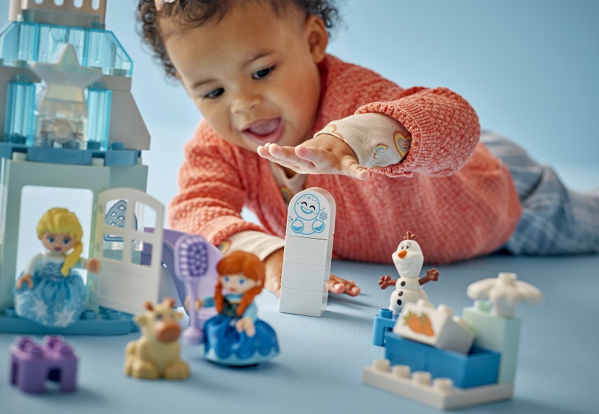 Malé dievčatko sa hrá na zemi so stavebnicou LEGO® DUPLO® Disney 10455 Ľadové kráľovstvo: Anna a Elsa a oslava na hrade.