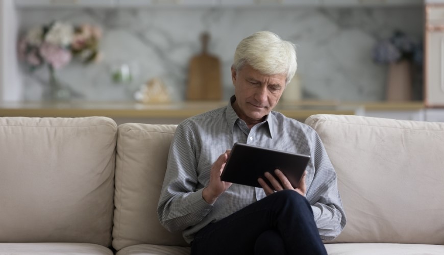 Ako vybrať tablet? starší muž sedí na pohovke a pracuje na tablete