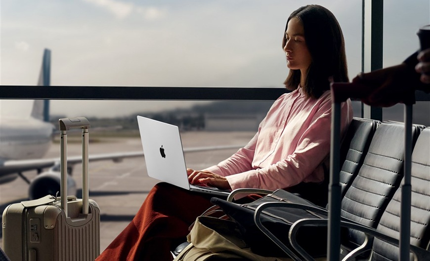 Ako vybrať notebook žena sedí v letiskovej hale na lavičke a pracuje na MacBooku Pro 14 M5, ktorý má položený na kolenách
