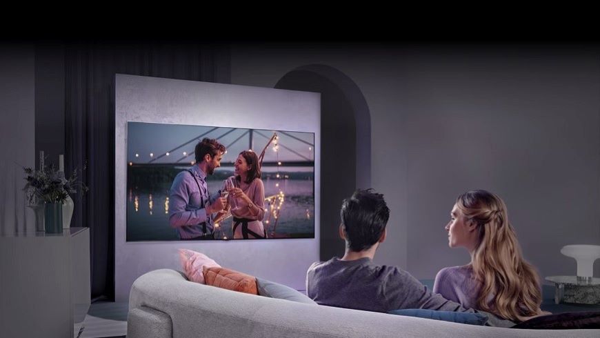 Muž a žena v obývačke sledujú televízor na stene.