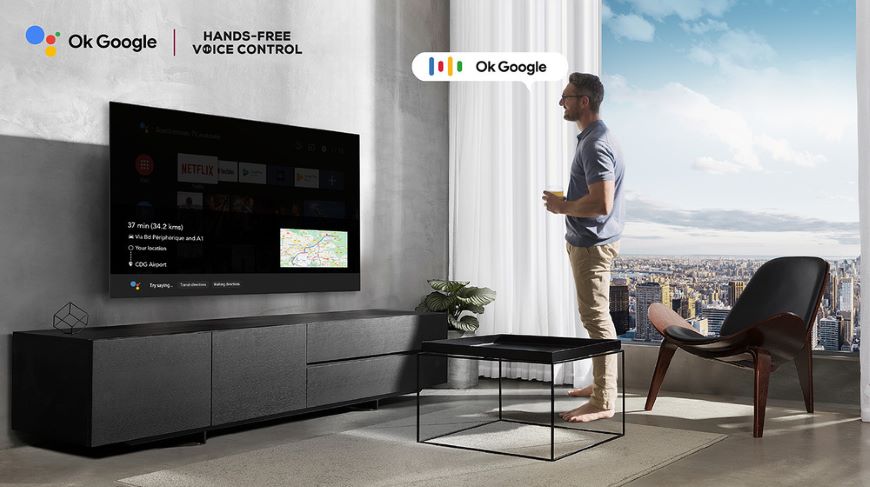 Muž stojí pred TV a v pozadí je výhľad na mesto.