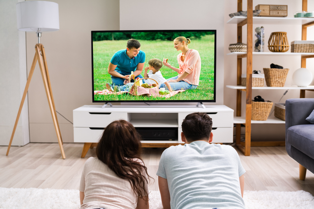 Muž a žena sledujú televízor s rodinnou scénou.